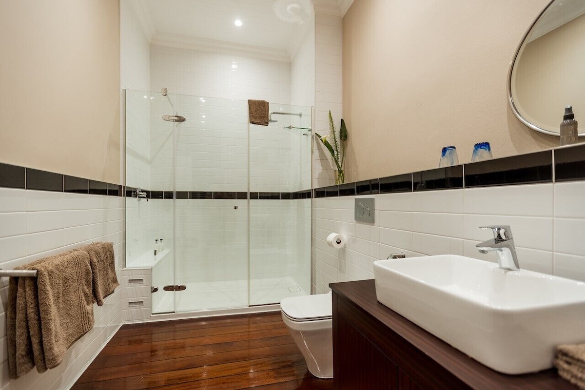 A modern bathroom with a glass-enclosed shower, a white sink, and a wooden floor.