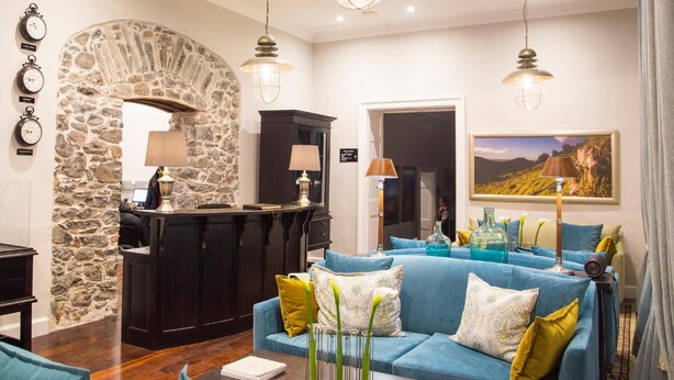 A modern hotel lobby with a stone archway, a reception desk, a blue sofa, and a painting on the wall. - Mantis St Helena (Jamestown)