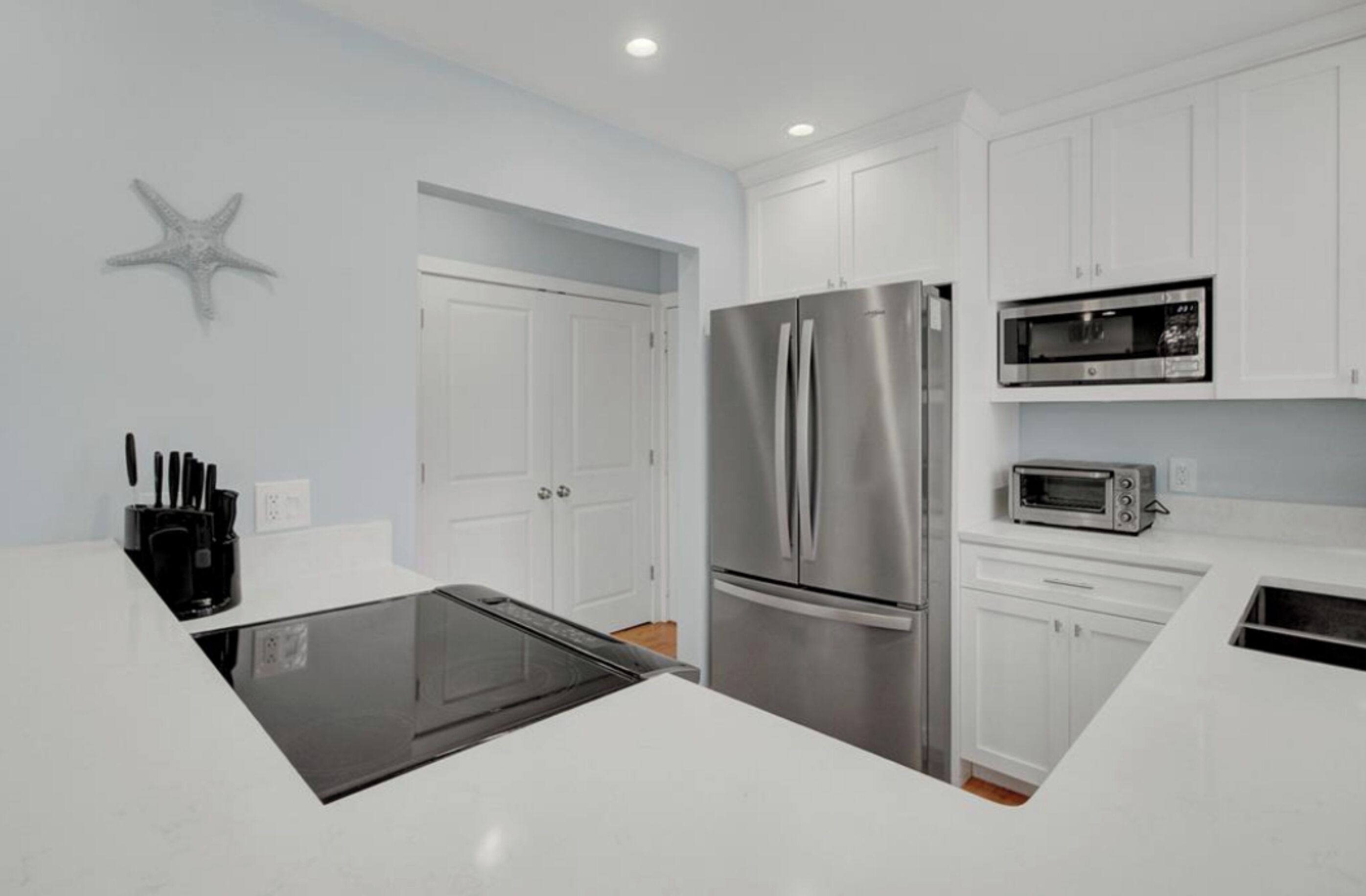 A modern kitchen with white cabinets, a stainless steel refrigerator, a microwave, and a black countertop.