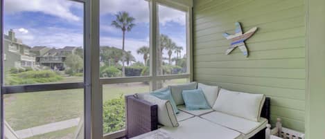 A covered outdoor seating area with a sofa and table, large windows, and a view of a residential area.