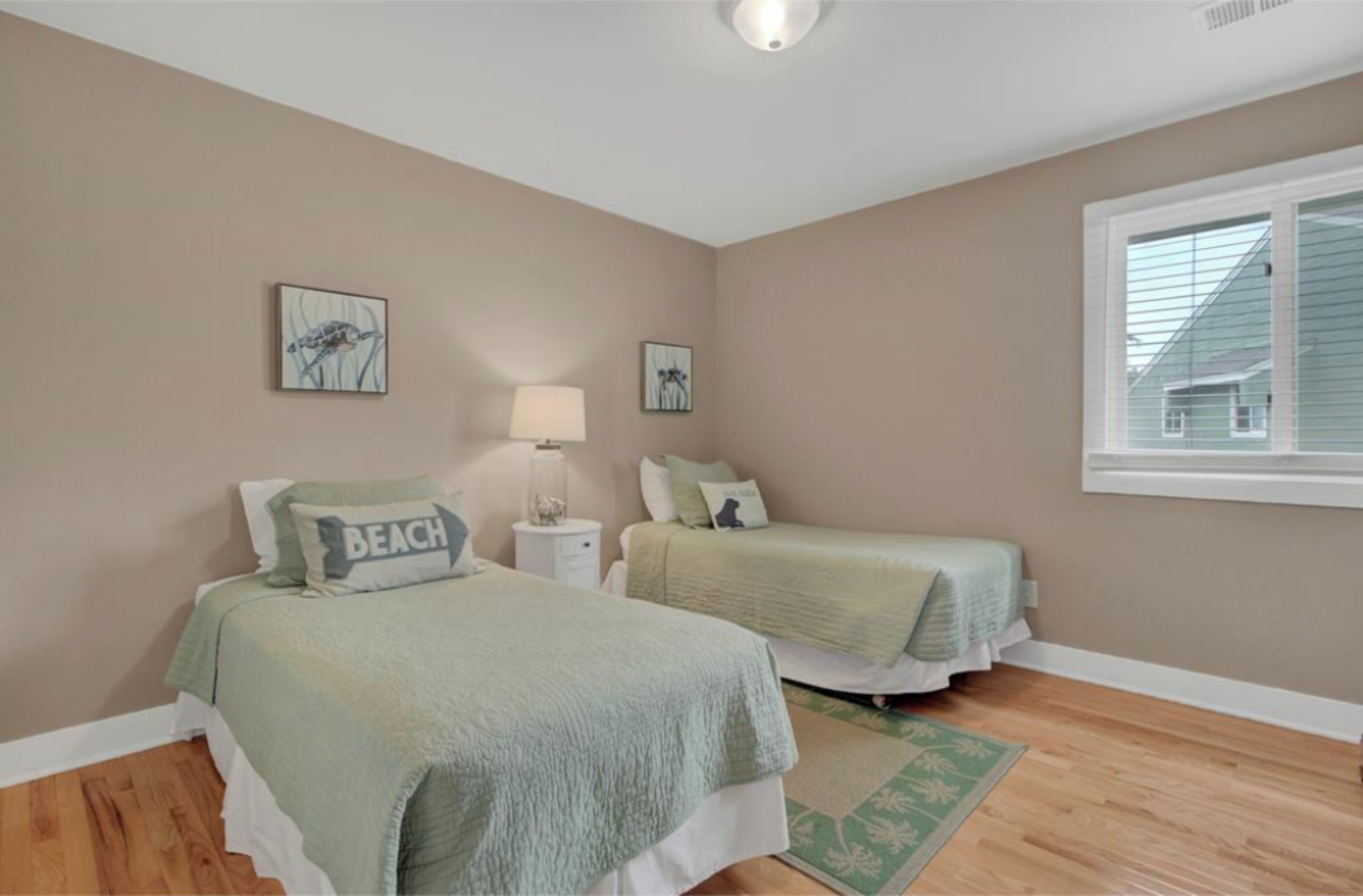 A bedroom with two beds, a window, and a green rug.