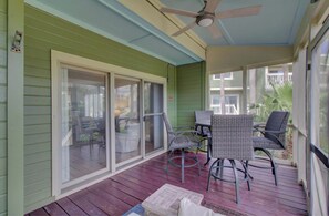 A covered porch with sliding glass doors, wicker furniture, and a ceiling fan.