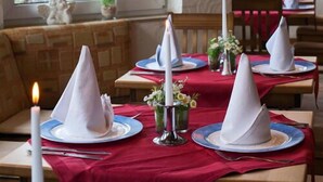 Een restaurant met gedekte tafels, rode tafelkleden en witte servetten.