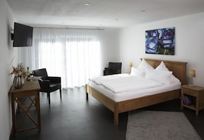 A modern bedroom with a wooden bed, a desk, a chair, a TV, and a painting on the wall.