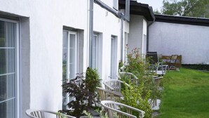 Een gebouw met een witte gevel, veel ramen en een kleine tuin met stoelen en planten.
