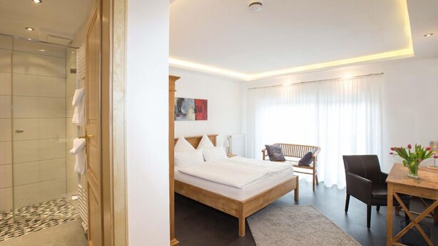 Een moderne hotelkamer met een groot bed, een douche, een eethoek met een tafel en stoelen, en uitzicht op de omgeving.