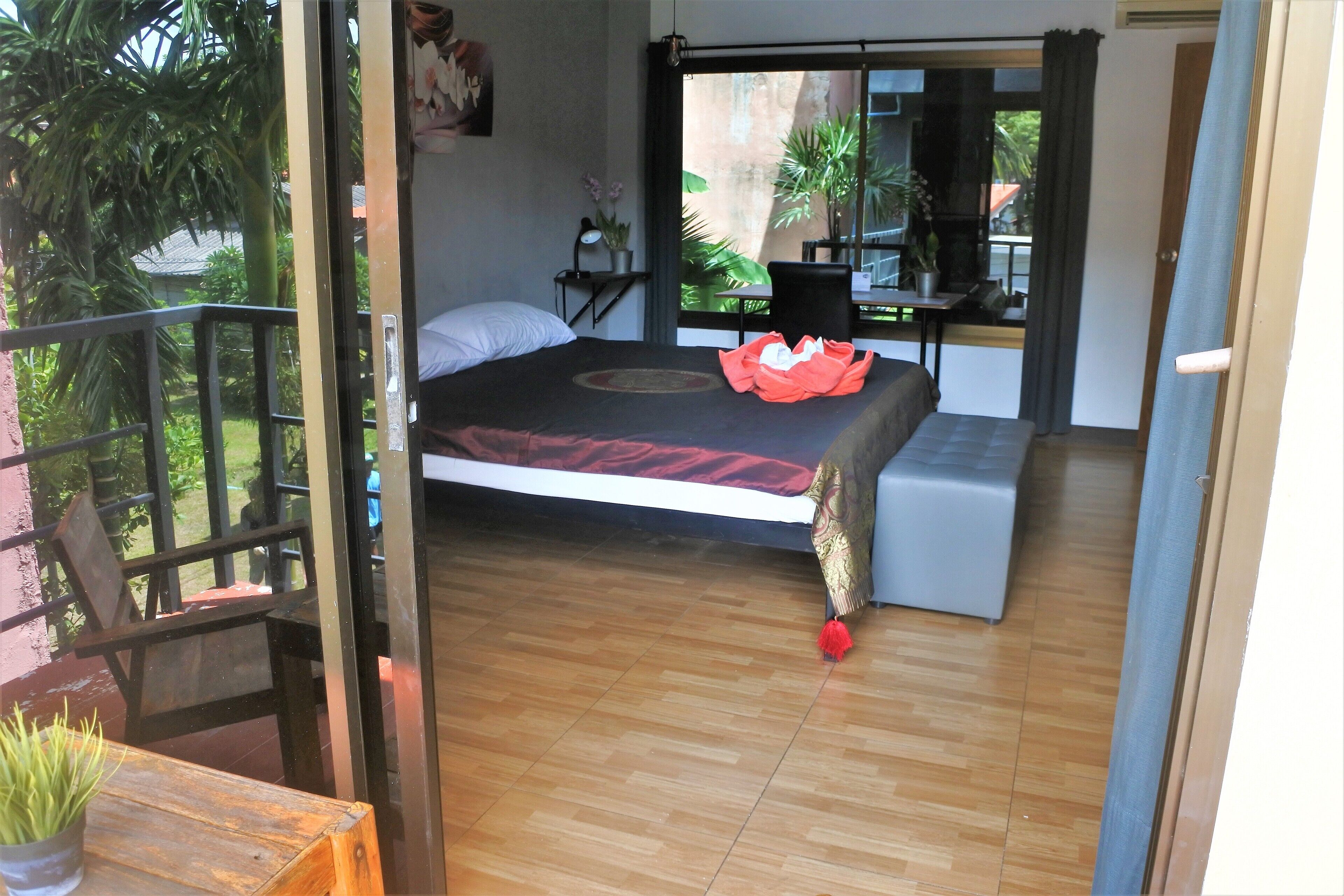 A bedroom with a bed, a small desk, a potted plant, and a balcony with a railing.