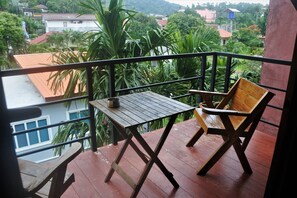 A balcony with a wooden table and chair, overlooking a residential area with houses and greenery. - Hi Karon Beach Hotel (Karon)