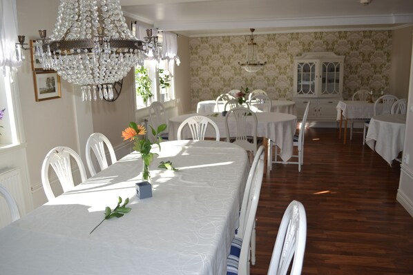 A dining area with a long table, white chairs, and a chandelier. There is a cabinet with glass doors in the background. - Mellanfjardens Pensionat (Jättendal)