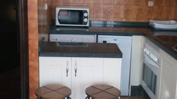 Een keuken met witte kastjes, een magnetron, een vaatwasser en twee krukken.