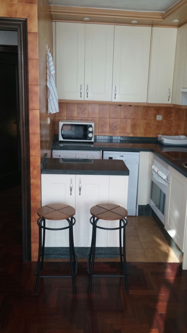 A kitchen with white cabinets, a microwave, a dishwasher, and two stools.