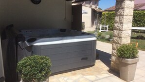 Een hottub onder een pergola, omgeven door stenen pilaren en plantenpotten.