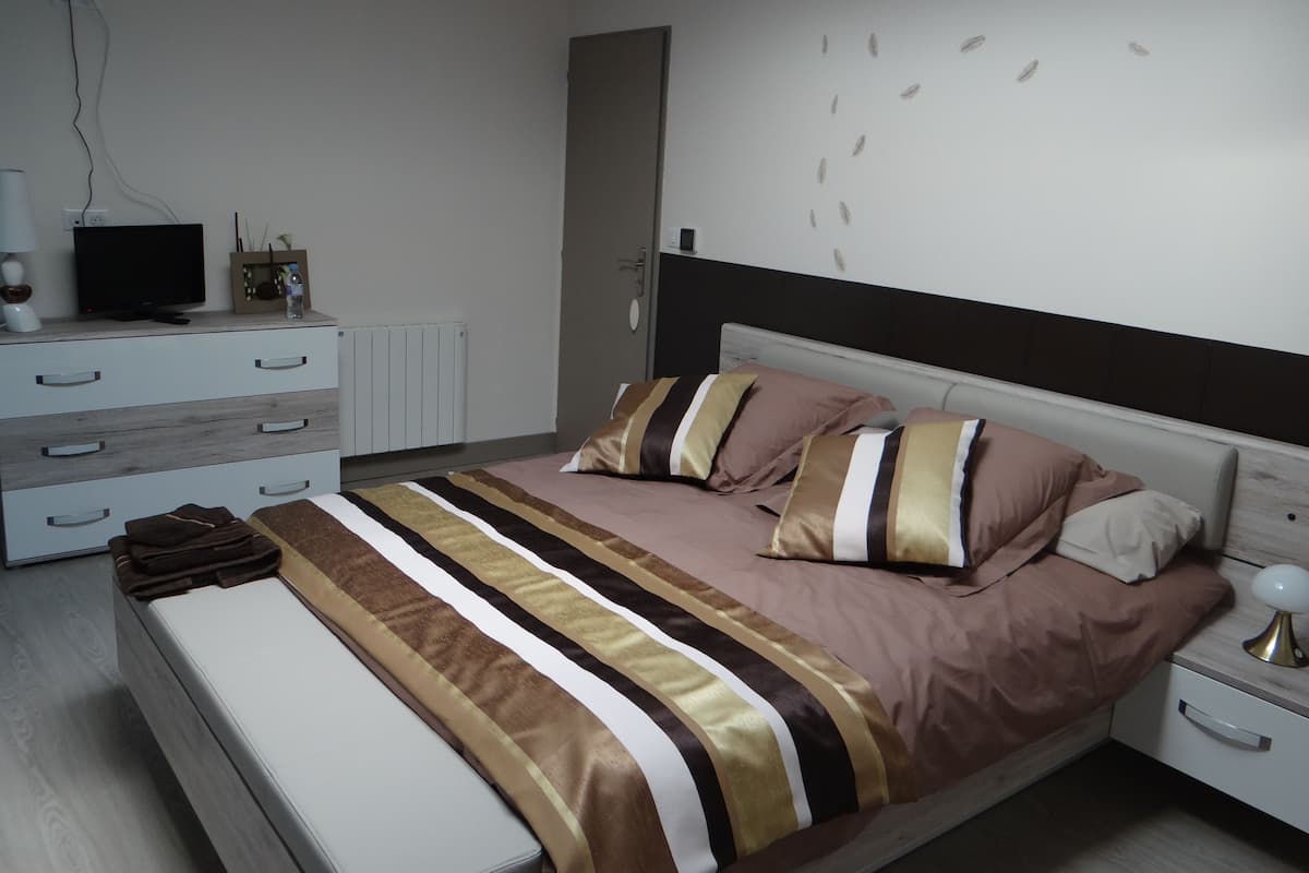Een moderne slaapkamer met een bed, nachtkastjes, een televisie en een radiator.