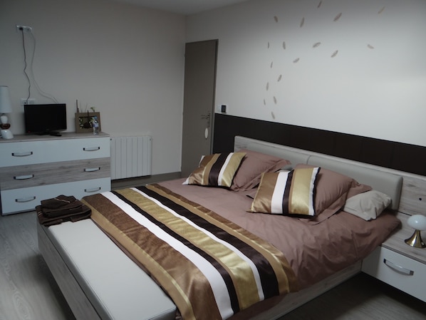 Un dormitorio moderno con una cama, mesitas de noche, un televisor y un radiador.