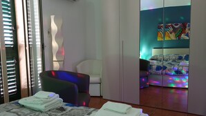 Ein Hotelzimmer mit Bett, Sessel, Kleiderschrank und farbenfroher Wanddekoration.