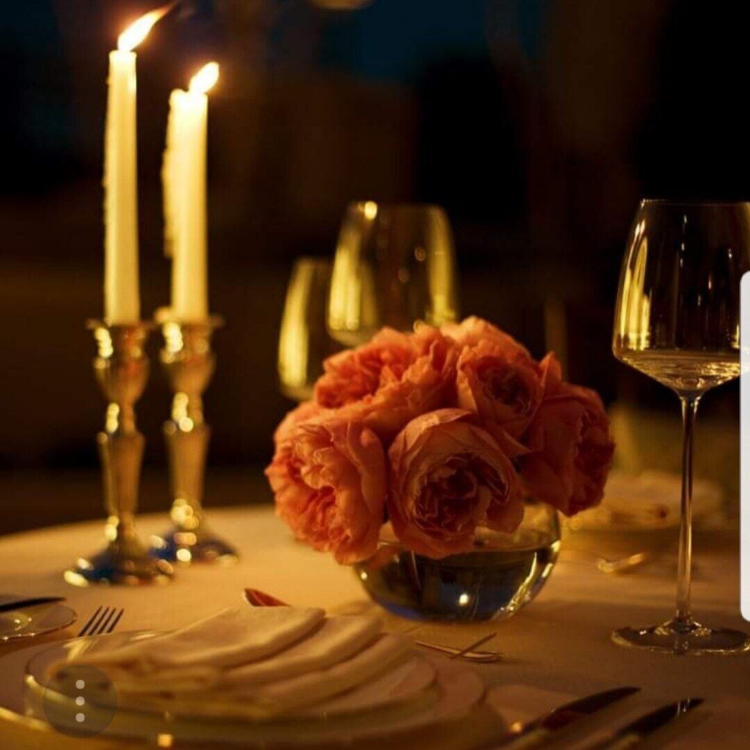 Ein Esstisch, gedeckt mit Kerzen, einer Blumenschale und Weingläsern.