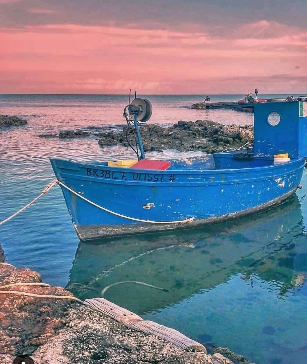 Un barco azul con el número de registro BR 3817 ULISSE # anclado cerca de costas rocosas.