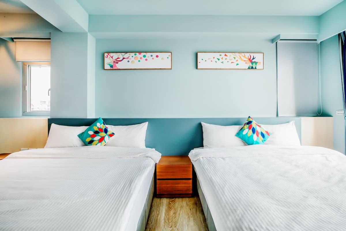 A hotel room with two beds, a wooden nightstand, and artwork on the wall.