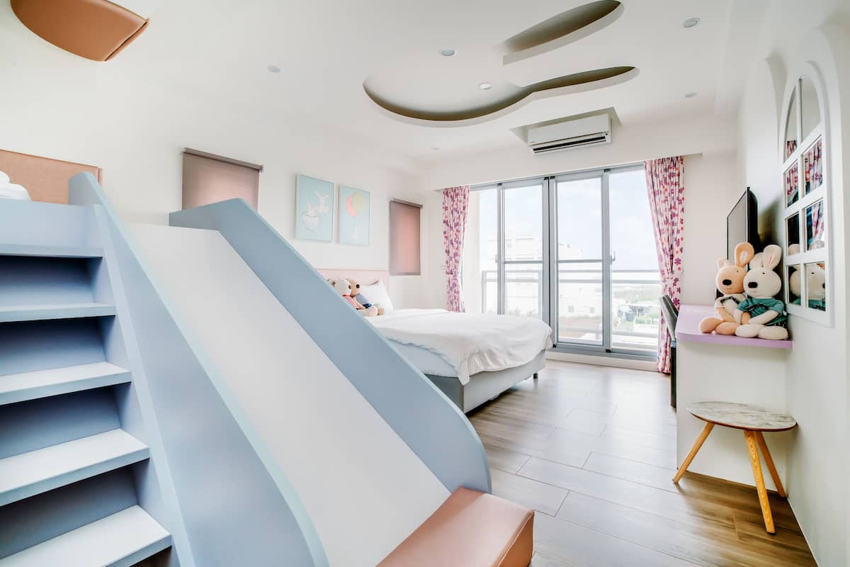A modern bedroom with a staircase, a bed, a window with curtains, and a small table.