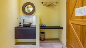Un baño con un espejo redondo, un lavamanos con un recipiente, una puerta de madera y un perchero.