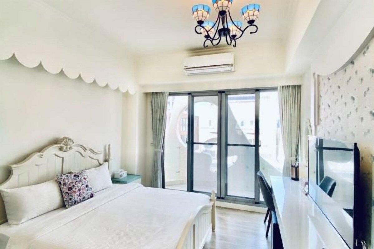 Una habitación de hotel con cama, televisión, balcón y candelabro.