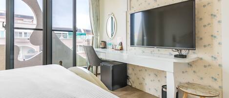 Une chambre d’hôtel avec un grand lit, un bureau avec un ordinateur, une télévision et une vue sur l’extérieur.