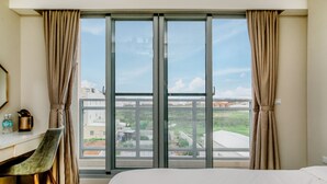 Habitación de hotel con cama, escritorio y vista de la ciudad a través de amplias puertas correderas de vidrio.