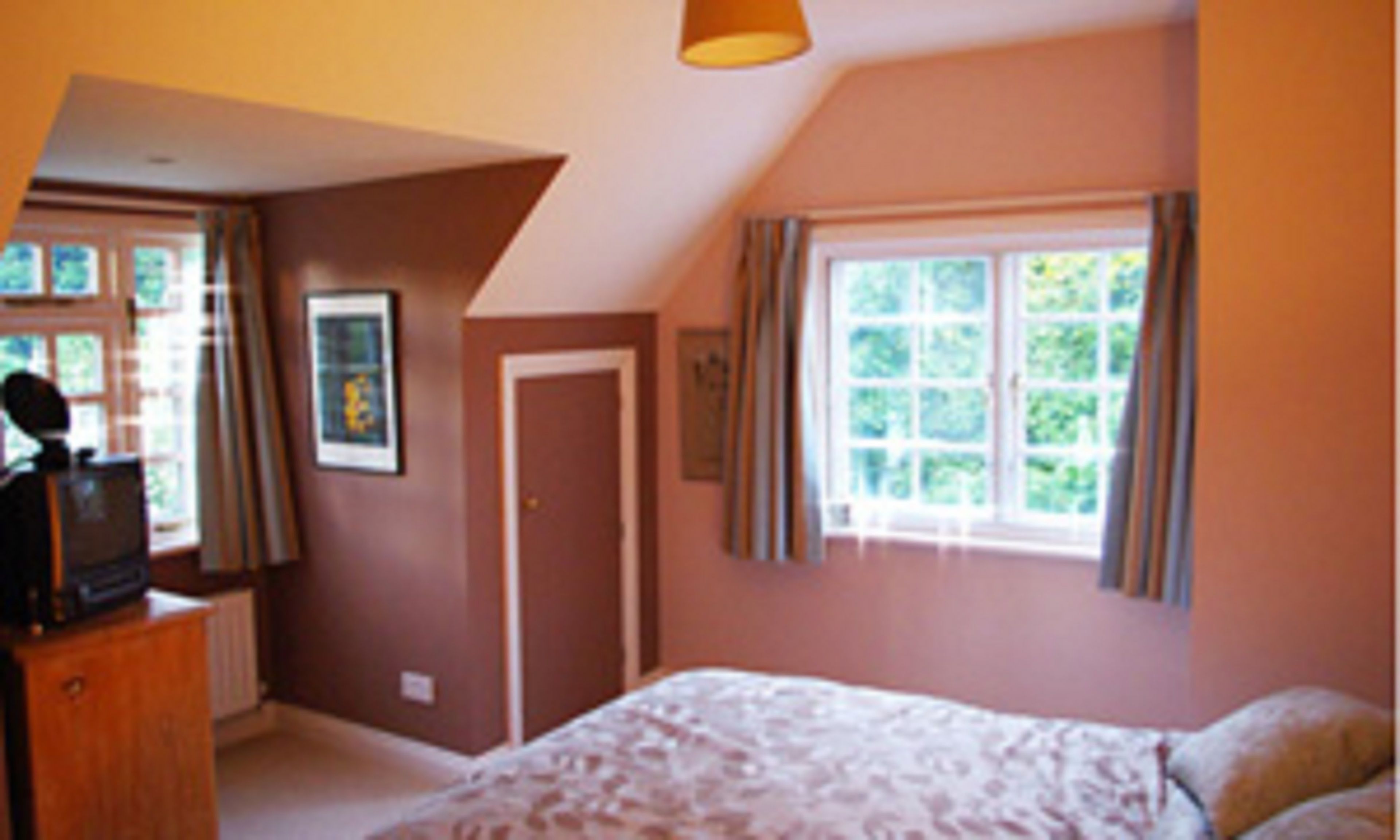 A bedroom with a bed, a desk, and a window with curtains.