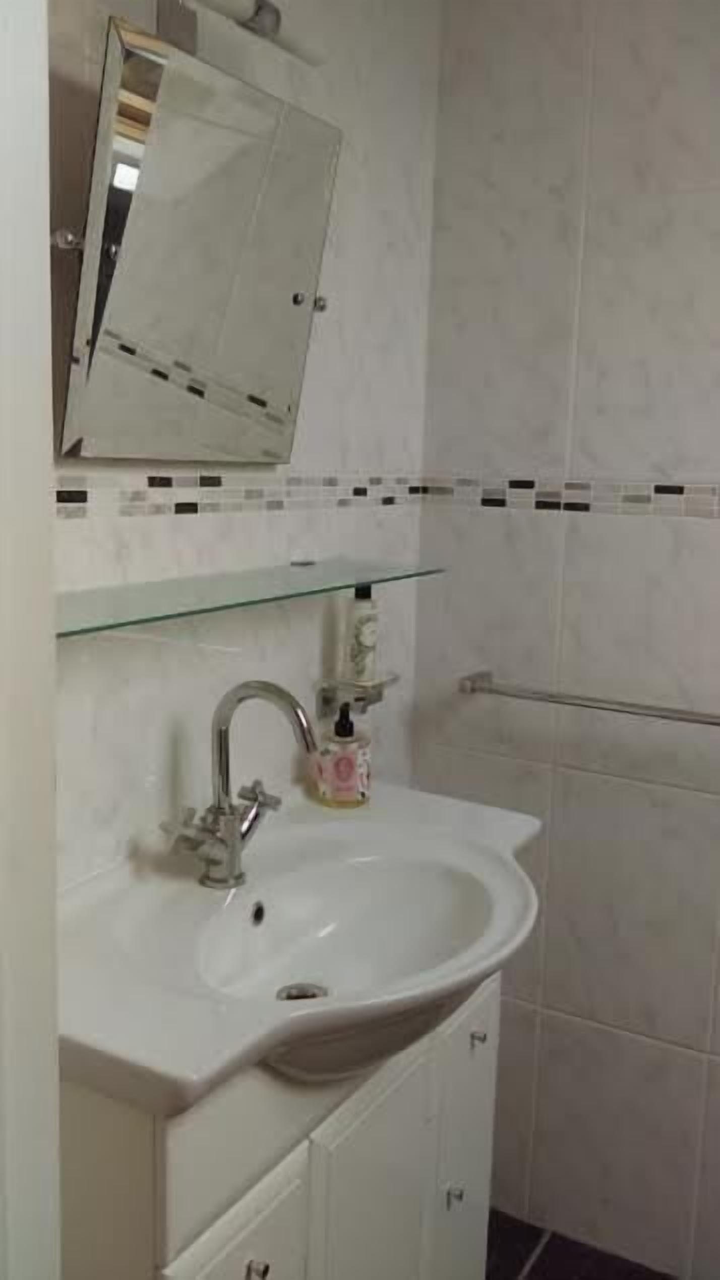Un baño con un lavabo blanco, un espejo y una repisa de vidrio sobre el lavabo.