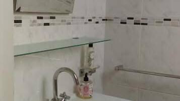 Un baño con un lavabo blanco, un espejo y una repisa de vidrio sobre el lavabo.