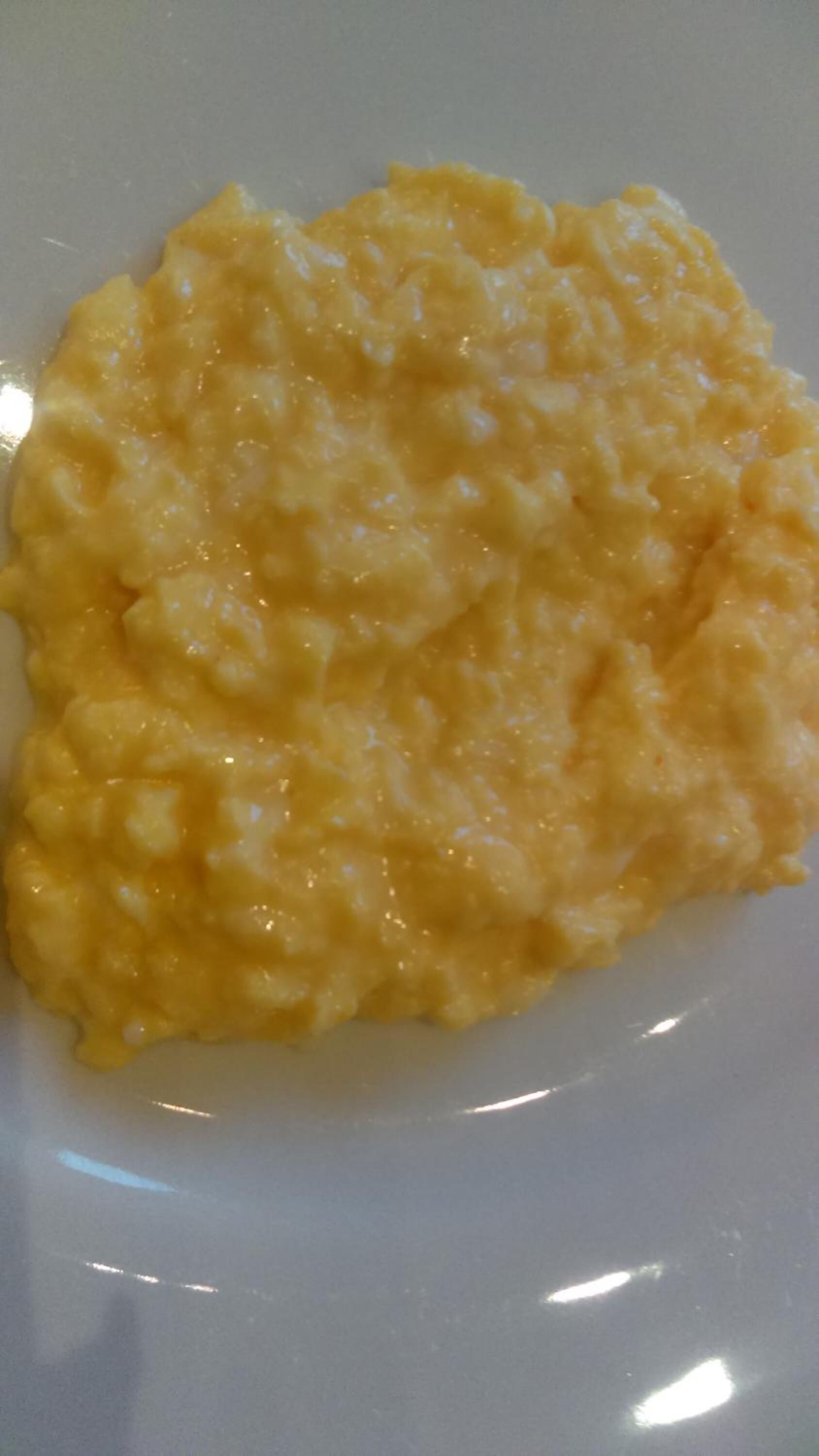 A close-up of a creamy yellow dish, possibly a type of risotto or porridge, on a white plate.