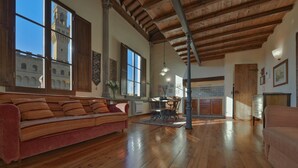 Un salon spacieux doté de parquets en bois, d’un canapé rouge et d’un coin repas avec une table et des chaises.