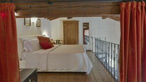 Une chambre avec un plafond en bois, un lit avec une literie blanche, un oreiller rouge et une vue sur un balcon doté d’une balustrade.