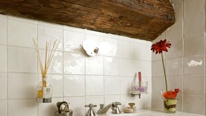 Une salle de bain avec un lavabo blanc, deux robinets, un miroir et un plafond en bois.