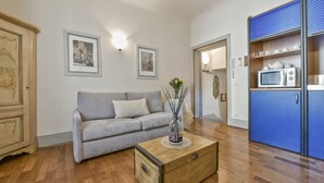 Un salon avec un canapé gris, une table basse en bois sur laquelle se trouve un vase, et un meuble bleu contenant un four à micro-ondes.