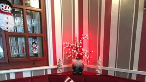 A red upholstered sofa with striped pillows, a round wooden table with napkins, and a decorative tree with lights. - Montgomery Hotel (Blackpool)