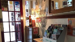 A reception area with a glass door, a fire extinguisher, a desk with a computer and brochures, and a mirror on the wall. - Montgomery Hotel (Blackpool)