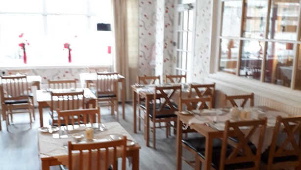 A dining area with wooden tables and chairs, a clock on the wall, and a television mounted above a window. - Montgomery Hotel (Blackpool)