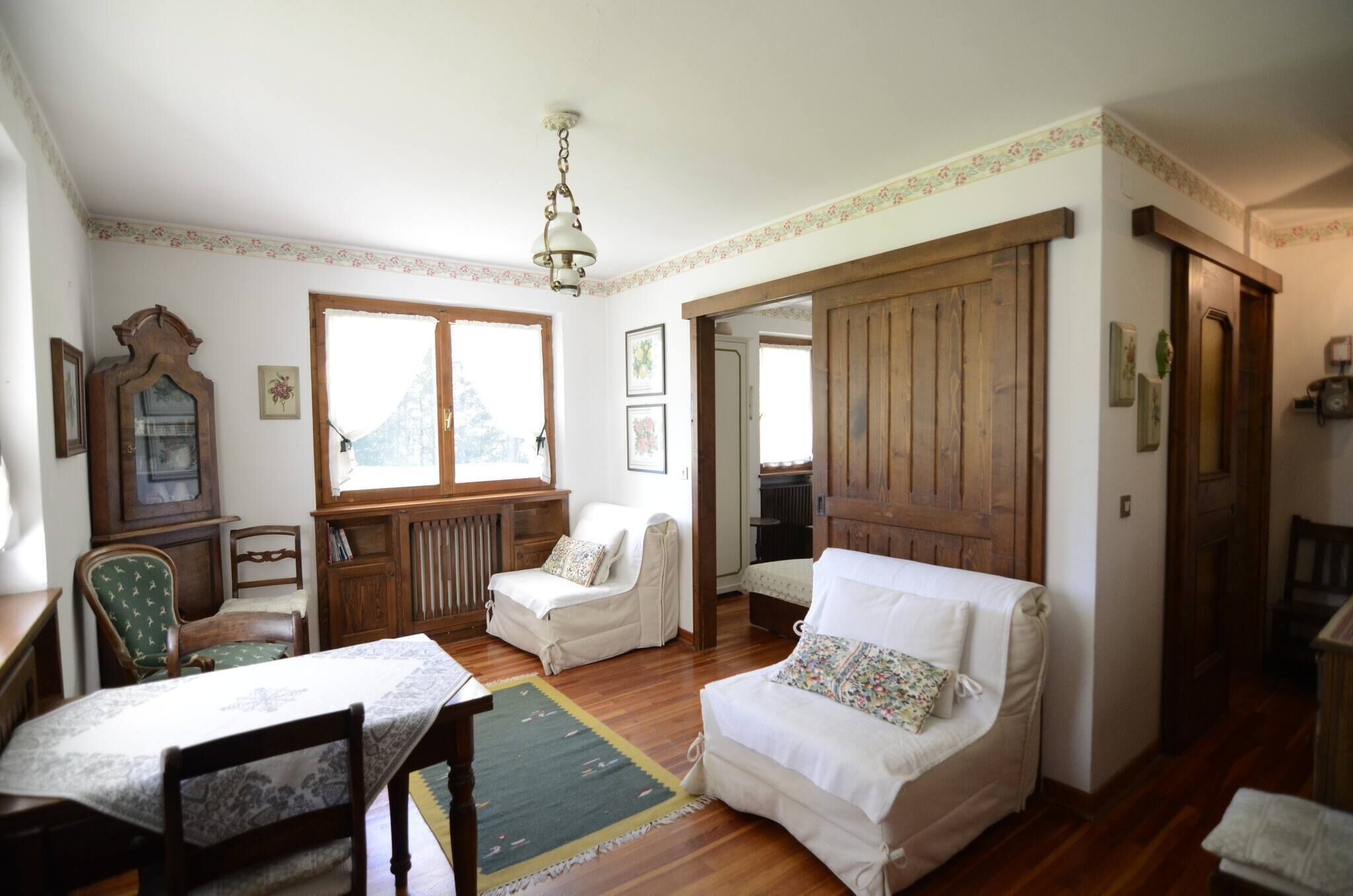 Quarto com piso de madeira, duas poltronas brancas, um armário de madeira e uma mesa com toalha.