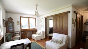 Une pièce avec un plancher en bois, deux fauteuils blancs, un buffet en bois et une table recouverte d’une nappe.