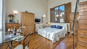 Une chambre à coucher avec un lit, un plancher en bois, un bureau avec une chaise, une télévision et une fenêtre avec des volets en bois.