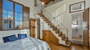 Une chambre avec un grand lit, un escalier en bois et une vue sur le paysage urbain par la fenêtre.