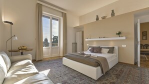 Ein modernes Schlafzimmer mit einem großen Bett, einer Couch, einem kleinen Tisch mit Obst und Blick auf ein Gebäude.