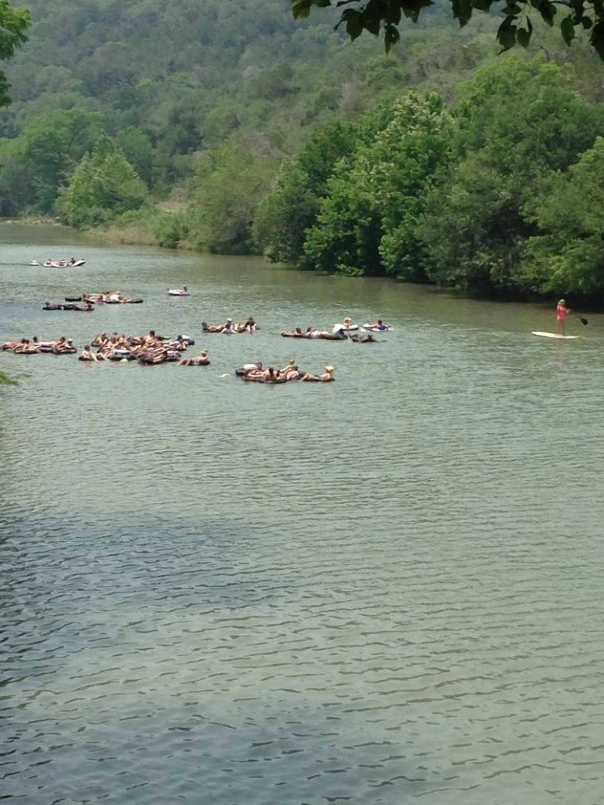 A river with people floating on rafts and one person paddleboarding.