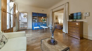 A spacious living area with a wooden floor, a white sofa, a coffee table with a decorative item, a TV, and a wooden cabinet. - Cozy Studio w/ Terrace & Unparalleled Location (Firenze)