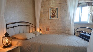 A bedroom with a stone wall, a bed with white bedding, a bedside table with a lantern, and a window with curtains. - Arnolongo Apartments (Rovinj)