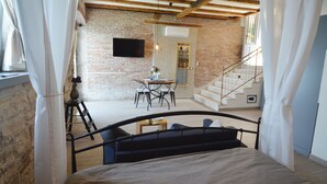 A bedroom with a bed, a small table, and a chair, a staircase, and a brick wall with a TV mounted on it. - Arnolongo Apartments (Rovinj)