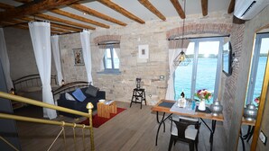 A cozy room with a bed, a dining table with chairs, a small table with a vase, and a window with a view of the water. - Arnolongo Apartments (Rovinj)