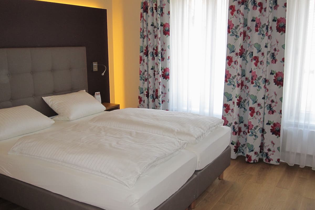 Ein Doppelbett mit weißer Bettwäsche in einem Hotelzimmer.