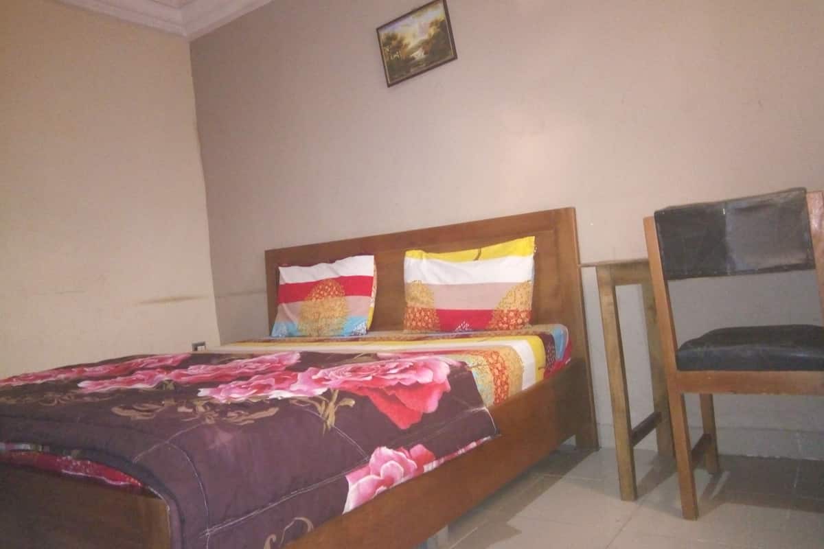 Una cama con colcha estampada, dos almohadas, un cabecero de madera y una mesita de noche con una silla.